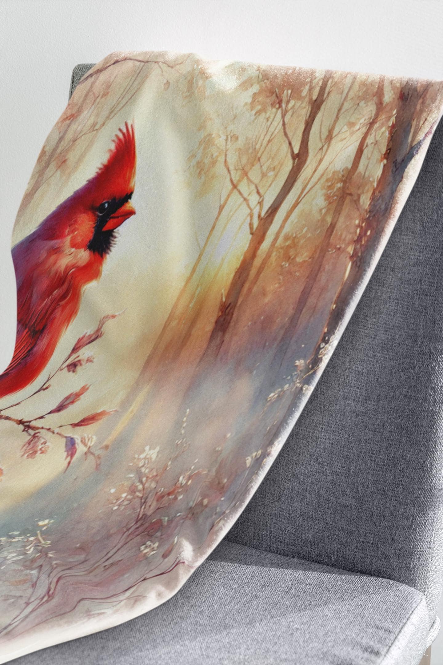 Soft blanket with a vibrant red cardinal and forest scene design draped over the back of a modern gray chair.