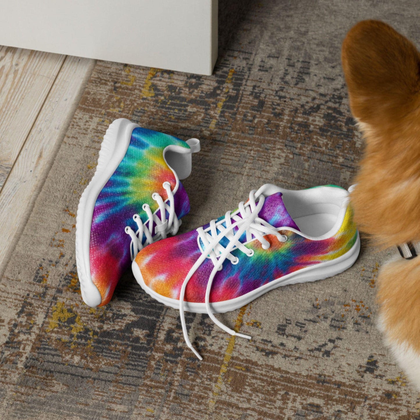 Pair of rainbow tie-dye sneakers with white soles and laces placed on a stylish rug near a curious dog—vibrant, comfortable footwear perfect for pet-friendly, casual lifestyles.