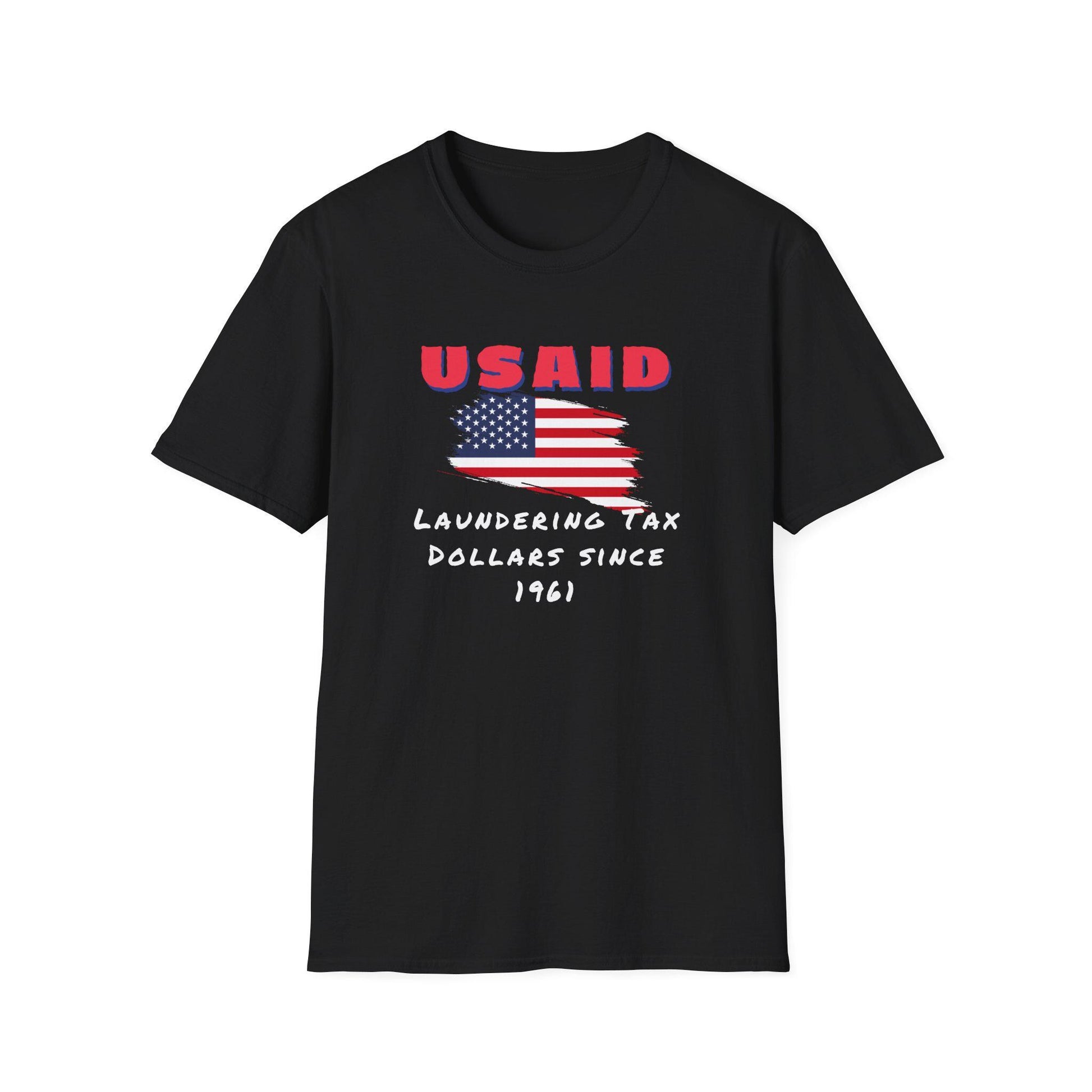 A black T-shirt is displayed flat against a white background. The shirt features a distressed American flag graphic in the center with bold red text above that reads &quot;USAID.&quot; Below the flag, white handwritten-style text says: &quot;Laundering Tax Dollars Since 1961.&quot; The design conveys a satirical political message with a rugged, protest-style aesthetic.