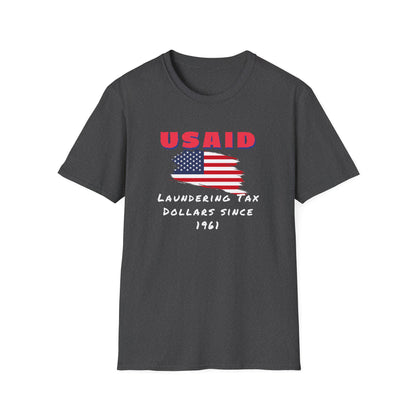 A dark heather gray T-shirt is displayed flat against a white background. The shirt features a bold graphic design with a distressed American flag in the center. Above the flag, red text reads &quot;USAID&quot; in all caps. Below, white handwritten-style text states: &quot;Laundering Tax Dollars Since 1961.&quot; The design has a satirical political tone with a rugged, protest-inspired aesthetic.
