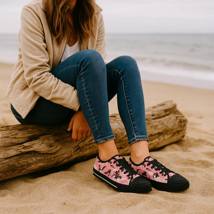 Woman sitting on driftwood at the beach wearing pink camouflage low-top sneakers with black laces, black toe caps, and rubber soles—stylish and comfortable footwear for casual coastal outings.