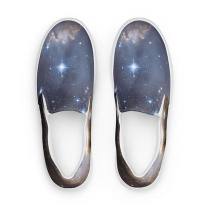 Top-down view of a pair of slip-on sneakers featuring a stunning galaxy print with stars, nebulae, and cosmic clouds in deep blues and subtle gold tones. The shoes have white elastic side panels and white soles, displayed against a clean white background.