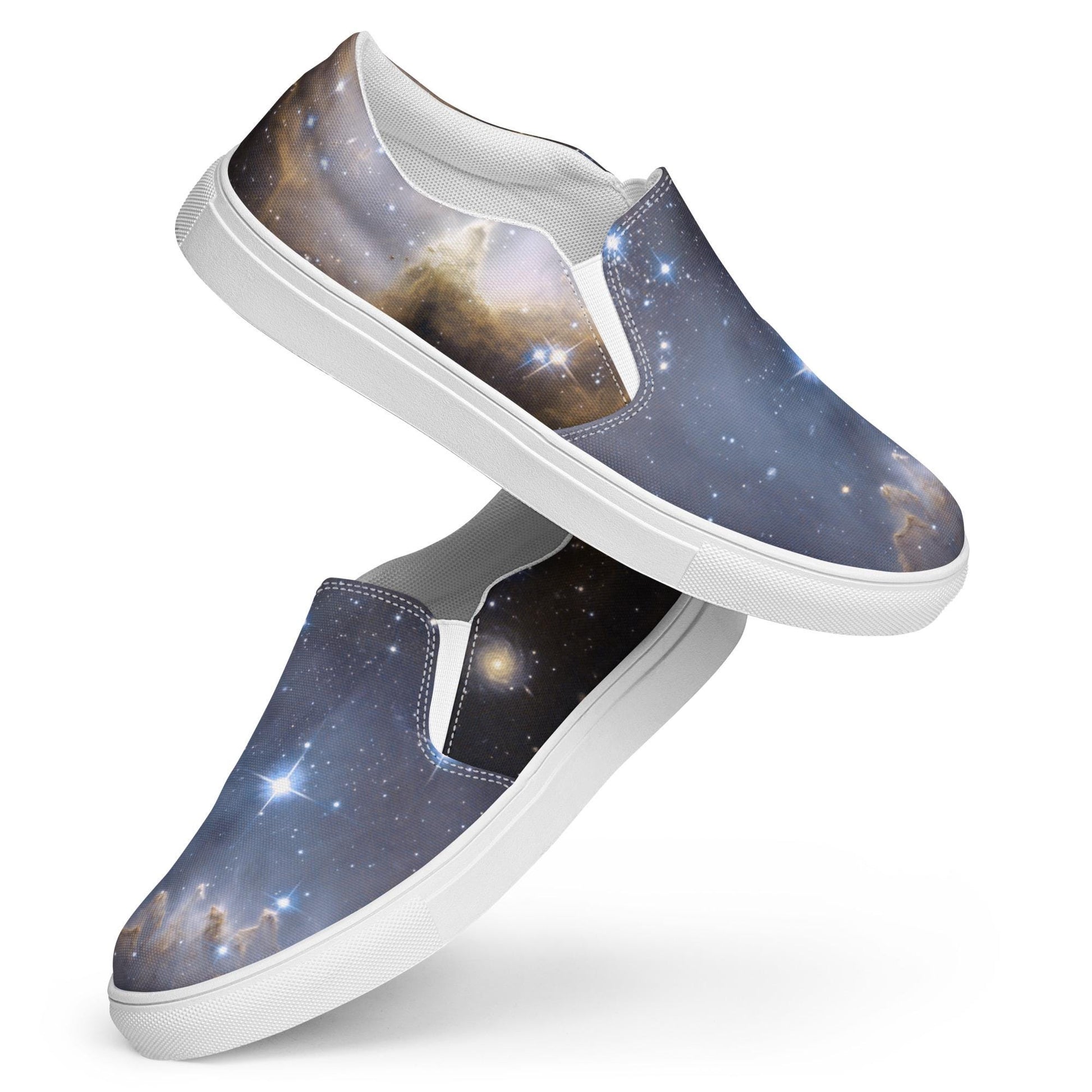 Pair of slip-on sneakers with a vibrant galaxy design featuring stars, nebulae, and cosmic clouds in deep blue, gold, and black hues. The shoes have white elastic side panels, white interiors, and white rubber soles. Displayed in a stylish stacked pose against a white background.