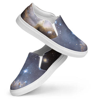 Pair of slip-on sneakers with a vibrant galaxy design featuring stars, nebulae, and cosmic clouds in deep blue, gold, and black hues. The shoes have white elastic side panels, white interiors, and white rubber soles. Displayed in a stylish stacked pose against a white background.