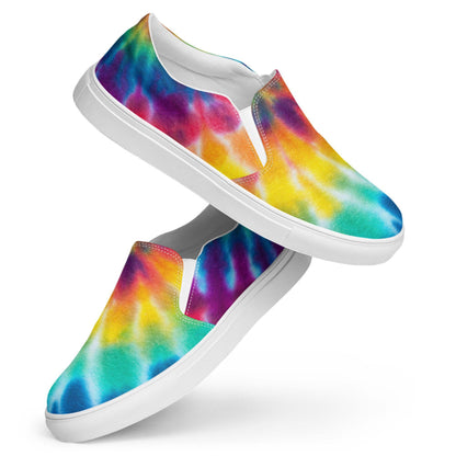 Floating display of colorful rainbow tie-dye slip-on canvas sneakers against a white background. These bold women’s casual shoes feature a vibrant watercolor pattern with turquoise, blue, yellow, orange, red, and purple hues. Designed with a sleek white rubber sole and elastic side panels for comfort and easy on/off wear.