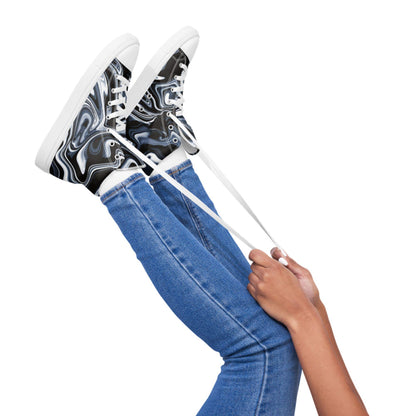 Person playfully holding up their legs while wearing high-top sneakers with a black, white, and blue marbled swirl pattern. The shoes feature white laces and white soles, paired with blue skinny jeans against a white background, creating a fun and dynamic studio-style image.
