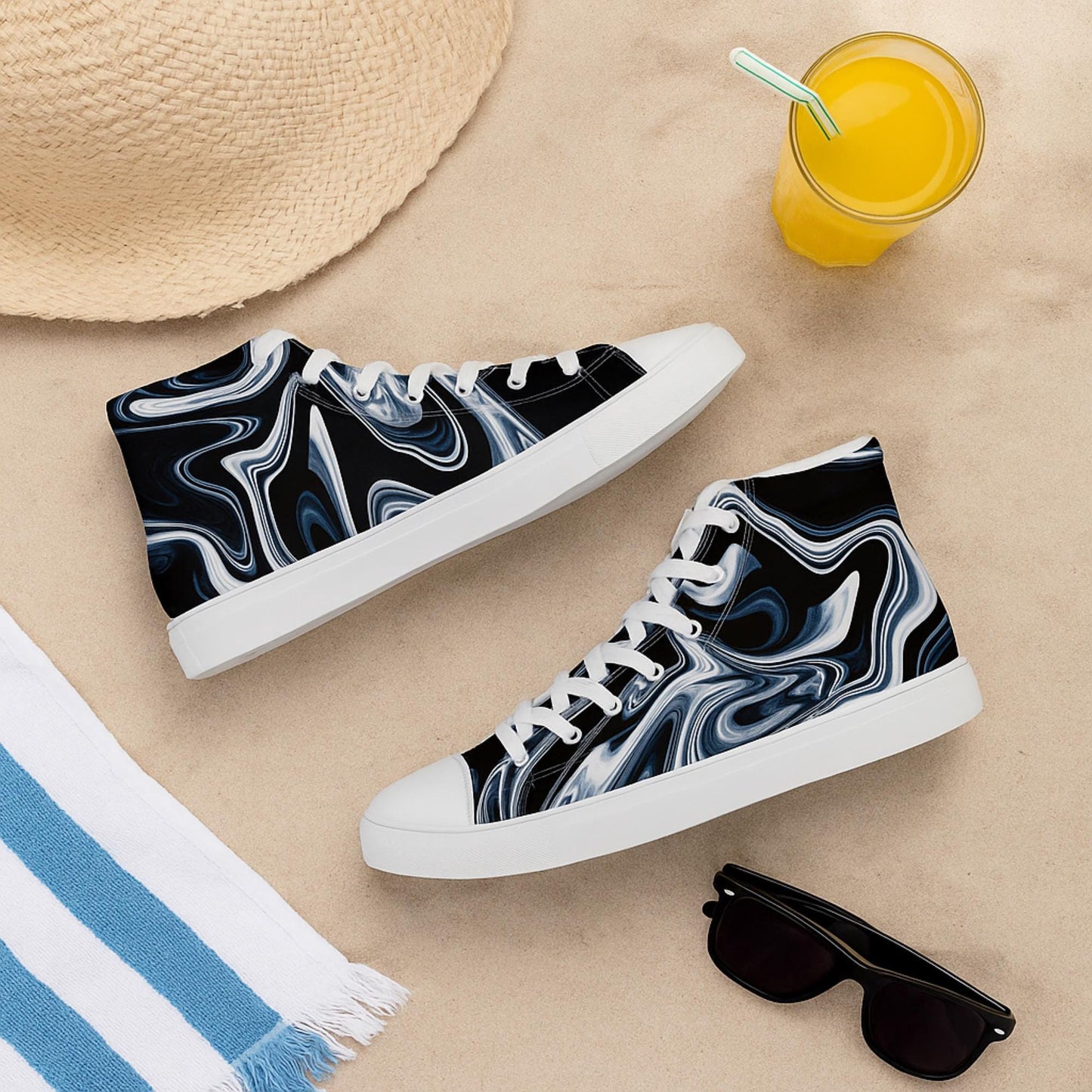 A pair of high-top sneakers with a black and white marbled swirl pattern and white soles and laces, displayed on sand. Surrounding the shoes are summer essentials: a woven straw hat, a blue-and-white striped towel, a glass of orange juice with a striped straw, and black sunglasses, evoking a relaxed beach or vacation vibe.