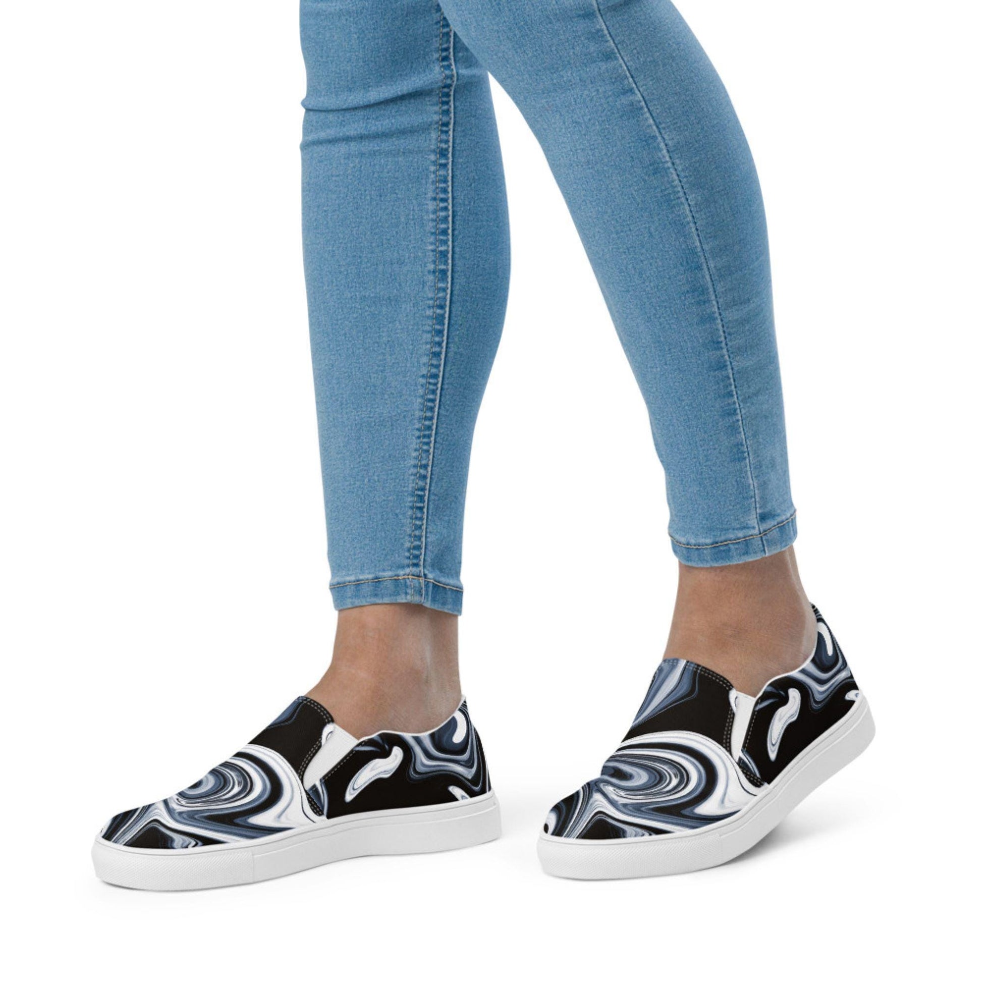 Close-up side view of a woman wearing slip-on canvas shoes with a black, white, and gray marbled swirl design, paired with light blue skinny jeans. Stylish and modern casual footwear for women, perfect for everyday fashion.