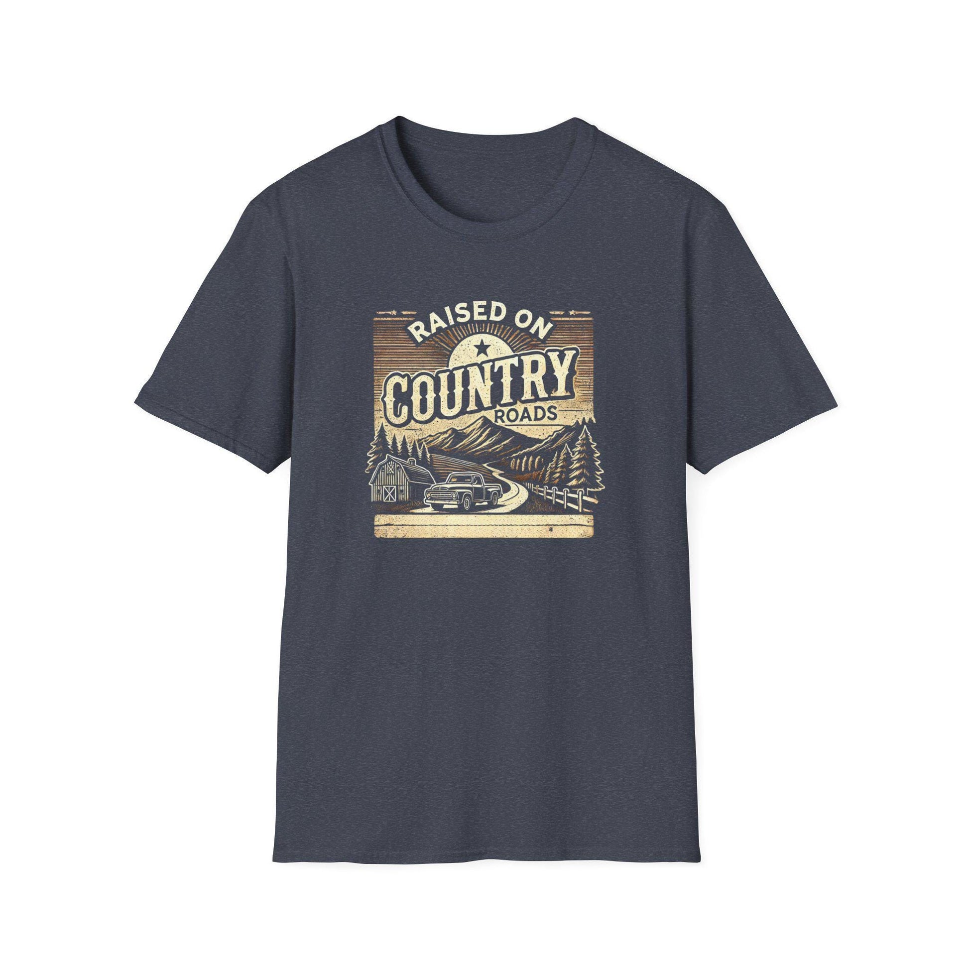 A heather navy unisex t-shirt is shown flat on a white background, featuring a retro-style design with the phrase &quot;Raised on Country Roads.&quot; The graphic includes a vintage pickup truck driving down a winding road through a scenic countryside with pine trees, a barn, mountains, and a sunrise. The artwork uses warm, earthy tones for a nostalgic and rustic aesthetic.