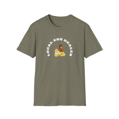 Olive green unisex t-shirt with a fun graphic of a cartoon hen sitting on a nest of eggs. The design features the phrase “LOCAL EGG DEALER” in bold white curved text above the illustration. The shirt is laid flat on a white background, highlighting its casual fit and crew neck style.