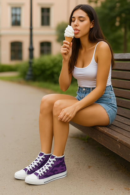 A young woman with long dark hair is sitting on a wooden bench in a park, wearing a white tank top, high-waisted denim shorts, and purple camouflage high-top sneakers with white laces. She is holding a vanilla ice cream cone and playfully sticking out her tongue to taste it, with her eyes closed. Trees and a light-colored building are visible in the background.