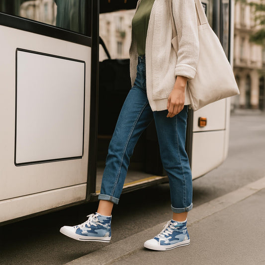 A woman steps onto a bus wearing cuffed blue jeans, a green top, a beige cardigan, and blue camouflage high-top sneakers. She carries a large off-white tote bag over her shoulder. The setting appears to be an urban street.