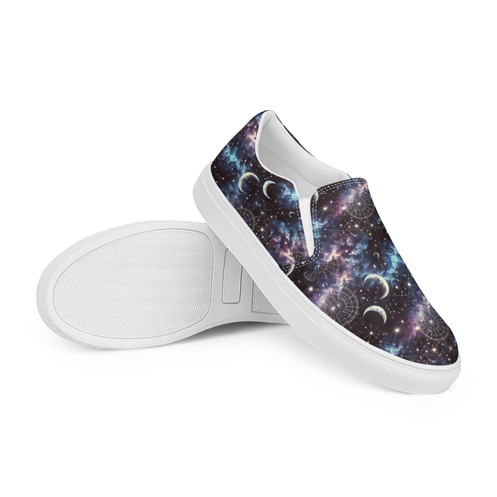Pair of slip-on canvas shoes with white soles featuring a vibrant galaxy-themed design. The pattern includes stars, nebulae, crescent moons, and celestial charts in shades of purple, blue, and black. One shoe is laid flat to display the sole&#39;s texture, while the other is positioned upright to showcase the outer design.