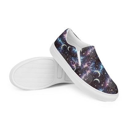 Pair of slip-on canvas shoes with white soles featuring a vibrant galaxy-themed design. The pattern includes stars, nebulae, crescent moons, and celestial charts in shades of purple, blue, and black. One shoe is laid flat to display the sole&#39;s texture, while the other is positioned upright to showcase the outer design.