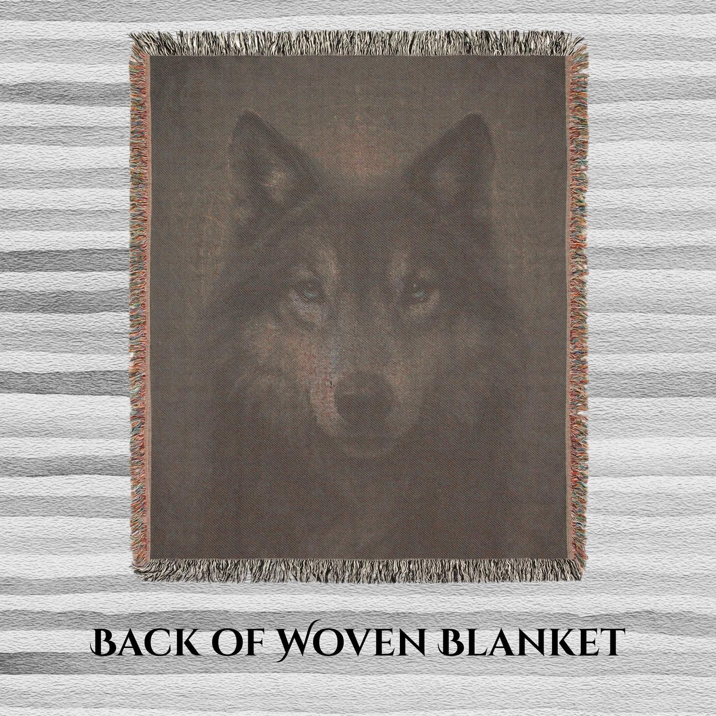 Back side of a woven blanket featuring a muted, reversed image of a wolf&#39;s face with visible thread texture. The blanket has multicolored fringe edges and is laid flat on a striped surface. Text at the bottom reads “BACK OF WOVEN BLANKET.”
