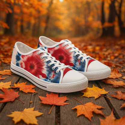 &quot;Pair of canvas sneakers with a vibrant red, white, and blue tie-dye design, featuring white laces and soles. The shoes are placed on a wooden path covered with autumn leaves, set against a forest backdrop with colorful fall foliage.&quot;