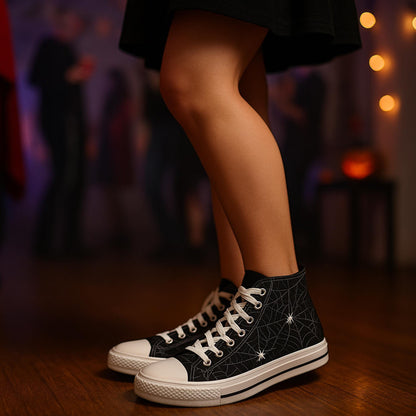 Close-up of a person wearing black high-top sneakers with a white spiderweb and spider design, standing indoors on a wooden floor. The person is dressed in a black skirt, and the background is softly blurred, showing people at a Halloween party with dim lighting and festive decorations.
