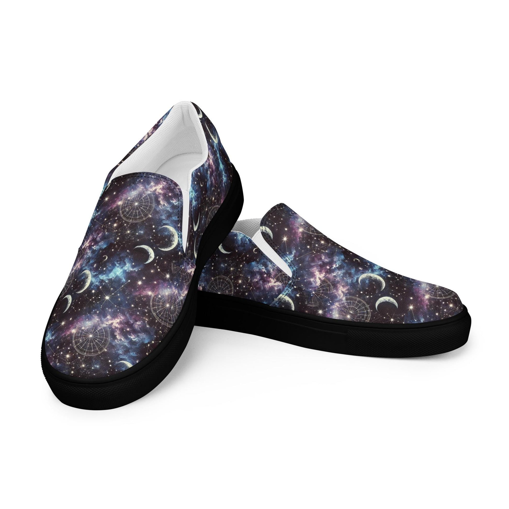 Pair of slip-on canvas shoes with black soles and a celestial galaxy design. The upper features a vivid space print with stars, nebulae, crescent moons, and astrological chart symbols in purple, blue, and black tones. One shoe is positioned upright and the other is slightly angled to display the full design and side view.