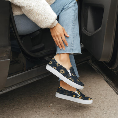 Woman sitting in an open car door wearing light blue jeans, a cozy cream Sherpa jacket, and navy slip-on shoes with a gold celestial star and moon pattern. Her legs are crossed as she rests her hand on her knee, highlighting the stylish footwear.