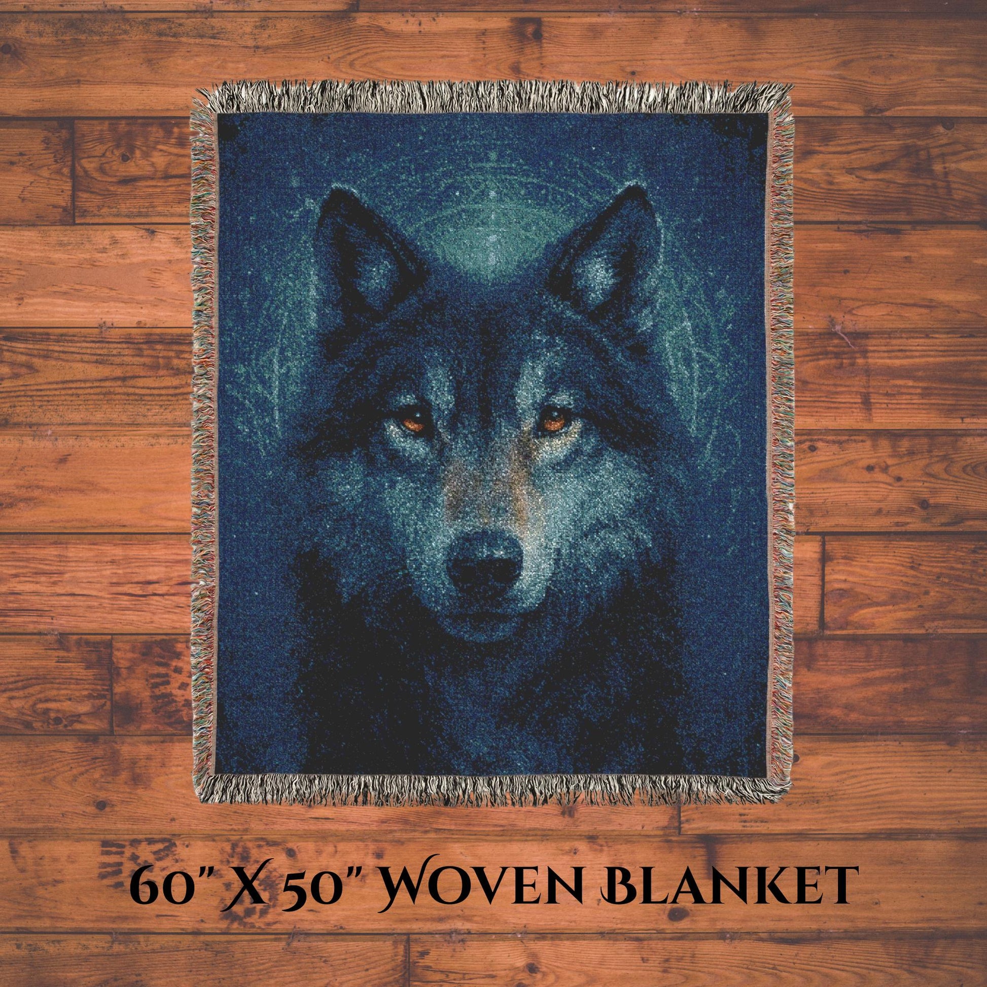 A 60&quot; x 50&quot; woven blanket featuring a detailed, realistic image of a wolf&#39;s face with piercing amber eyes. The blanket is laid flat on a wooden floor, showcasing its size and multicolored fringed edges. Text at the bottom reads “60&#39;&#39; X 50&#39;&#39; WOVEN BLANKET.”