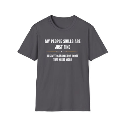 Dark gray unisex T-shirt laid flat on a white background, featuring bold white and gold text that reads: “MY PEOPLE SKILLS ARE JUST FINE — IT’S MY TOLERANCE FOR IDIOTS THAT NEEDS WORK.” The design includes a small decorative divider between the two lines for added visual interest.